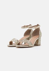 Guldklackade sandaler med glittrande övre, öppen tå och fotledsband. Klackarna är täckta med matchande glitter för extra textur.