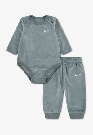 Miękki szary body niemowlęcy z długim rękawem oraz pasujące spodnie z subtelnymi wytłoczonymi logo Nike swoosh i białymi logo Nike.