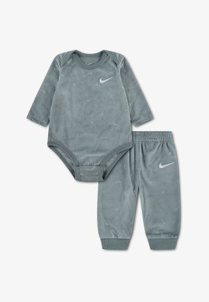 Miękki szary body niemowlęcy z długim rękawem oraz pasujące spodnie z subtelnymi wytłoczonymi logo Nike swoosh i białymi logo Nike.