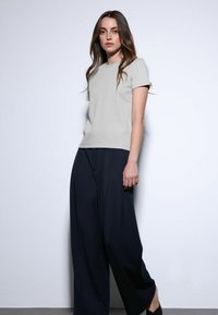 Lichtgrijs T-shirt met korte mouwen gecombineerd met losse, donkerblauwe broek. Gladde stoftextuur, minimalistisch ontwerp en neutraal kleurenpalet.