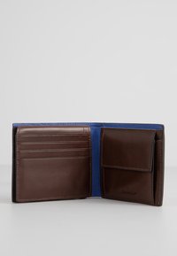 Interno di un portafoglio in pelle marrone con accenti blu, dotato di numerose fessure per carte, una tasca per monete e una texture liscia. Design a chiusura.