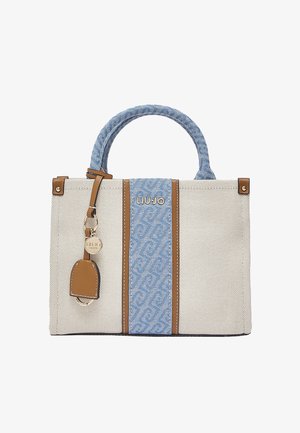 Bolso de tela beige con panel central y asa de patrón azul, detalles en cuero marrón y un charm redondo de marca en tono dorado.