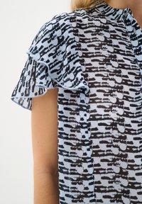 Camicia blu e nera a motivi con maniche arricciate, dotata di scollo rotondo e tessuto testurizzato con linee orizzontali alternate e cerchi.