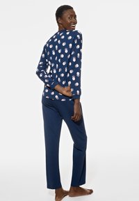 Ensemble de pyjama bleu marine comprenant un haut à manches longues et un pantalon, orné d'un motif circulaire rose. Tissu lisse, coupe décontractée et col ras du cou.