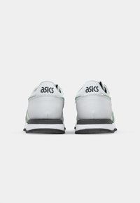 Sivé a biele tenisky so zelenými akcentmi. Majú textúrovaný zvršok, polstrovaný golier a čiernu gumovú podrážku. Na päte je značka ASICS.