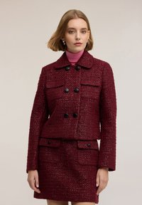 Burgundské texturované sako se dvěma předními kapsami, dvouřadým zapínáním na knoflíky a límečkem, doplněné o odpovídající sukni.