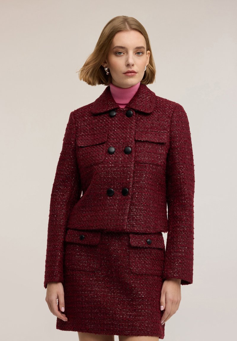 Burgundské texturované sako se dvěma předními kapsami, dvouřadým zapínáním na knoflíky a límečkem, doplněné o odpovídající sukni.