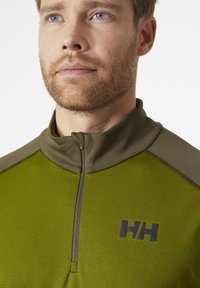 Zelený fleecový svetr s vysokým límcem, funkčním zipem a texturovanou tkaninou. Černé logo na hrudi, kontrastní akcenty na ramenech.