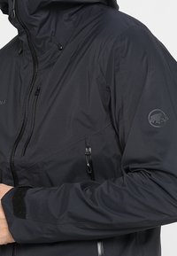 Sort vandtæt jakke med hætte, der har lynlåslommer, tekstureret stof og et logopatch på skulderen.