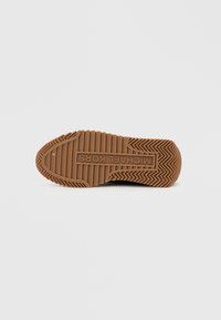 Λαστιχένια σόλα παπουτσιού σε ανοιχτό καφέ χρώμα με υφή που διαθέτει διαγώνιες αυλακώσεις και ορθογώνια πινακίδα με το λογότυπο «MICHAEL KORS» χαραγμένο.