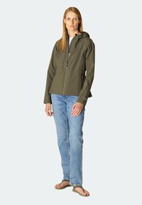 Chaqueta softshell verde oliva con cremallera frontal y capucha, combinada con jeans azul claro y chanclas. Cuenta con bolsillos laterales y un diseño elegante.