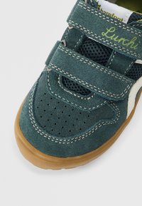 Roheline seemisnahast king võrgust paneelidega, kahe takjakinnitusega, auguline varvasteosa ja pruun kummist tald. Omaduseks valged aktsendid ja kontrastsed õmblused.