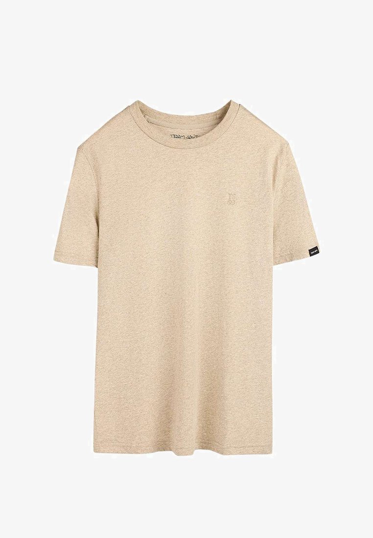 T-shirt beige à manches courtes et col rond, avec un logo de marque discret sur la poitrine et une petite étiquette noire sur la manche gauche.