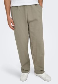 Pantalon de survêtement vert olive clair en tissu doux, avec une taille élastique, des poches latérales et une coupe droite.