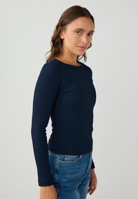 Marineblauwe geribbelde langetijdshirt met een ronde halslijn, getailleerd ontwerp en een gladde textuur, gecombineerd met hoge taille blauwe jeans.