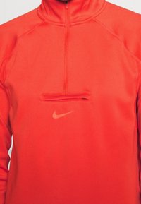 Roter Sportpullover von Nike mit hohem Kragen, halbem Reißverschluss und kleinem Logo in Hellorange. Glatte Textur mit kontrastierenden Nahtdetails.