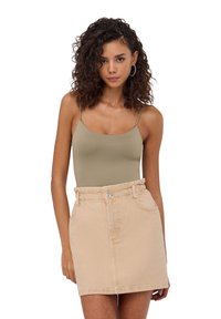 Gonna mini in denim beige con vita alta e tasche laterali, abbinata a una canotta aderente verde oliva con spalline sottili.