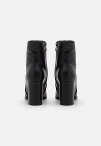 Paire de bottines en cuir noir à talons carrés, vues de dos sur un fond blanc.