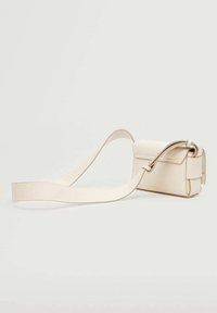 Pequeño bolso cruzado de cuero beige con una correa larga y ancha, colocado sobre un fondo claro y sencillo.