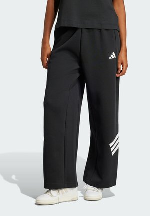 Pantalones de chándal negros de tela suave, con un ajuste holgado, dos bolsillos laterales y tres rayas blancas en la pierna izquierda.