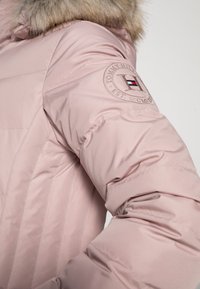 Hellrosa Daunenjacke mit gefütterter Kapuze, gestepptem Design und gesticktem Logo am Ärmel mit einer Farb-Akzentuierung.