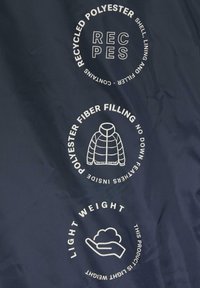 Navy stof met drie witte cirkellabels: "Gerecycled Polyester," "Polyester Vezel Vulling," en "Lichtgewicht," met relevante iconen.