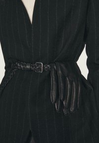 Czarny płaszcz w pionowe paski, z plecionym skórzanym paskiem i wsuniętymi czarnymi skórzanymi rękawiczkami w talii. Widoczny detal z teksturowanej tkaniny.