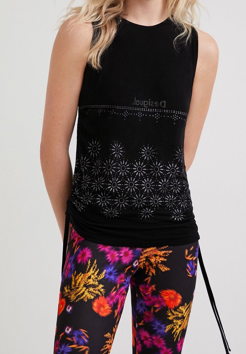 Femme portant un haut noir sans manches avec un motif floral découpé et des leggings à motif floral coloré.