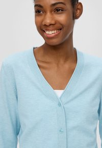 Jasnoniebieski kardigan z dekoltem w serek, prążkowanym kołnierzem i trzema guzikami. Materiał wydaje się miękki, o gładkiej fakturze i dopasowanym kroju.