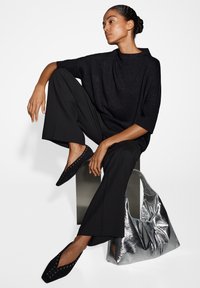 Top noir en tricot à manches courtes, pantalon noir ample, chaussures plates noires avec des détails en clous, et un sac hobo en argent brillant.