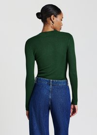 Grünes, geripptes Langarmoberteil mit rundem Halsausschnitt, kombiniert mit hochtaillierten blauen Jeans. Hervorzuheben sind die Textur und das figurbetonte Design.