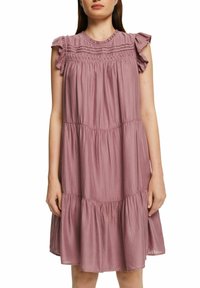 Robe sans manches de couleur mauve clair avec des épaules volantées, un corsage froncé et un ourlet à plusieurs niveaux. Tissu doux et texturé avec une coupe décontractée.