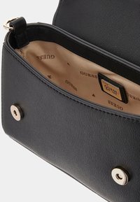 Black leather handbag with a textured finish. Interior shows beige lining embossed with "GUESS" logo, featuring metal snap closure.