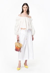 Top bianco off-the-shoulder con maniche voluminose, abbinato a una lunga gonna bianca. Presenta una borsa a secchiello marrone e arancione con dettagli in paglia.