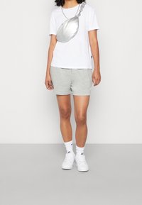 Bílá tričko, šedé šortky, stříbrná crossbody taška s řetízkem, bílé tenisky a bílé ponožky s černým logem.