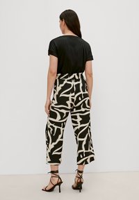 T-shirt nero a maniche corte abbinato a pantaloni beige a vita alta con un audace motivo astratto nero e sandali neri con cinturini.