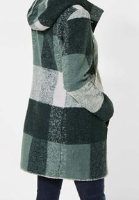 Grön rutig ullkappa med huva, i olika nyanser av grönt och grått, mjuk textur och midjelång design.