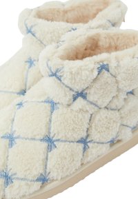 Cremefarbene Hausschuhe mit plüschiger Textur, die ein diamantgeplüstertes Design und blaue Nähte aufweisen. Weiche Innenpolsterung für Komfort.