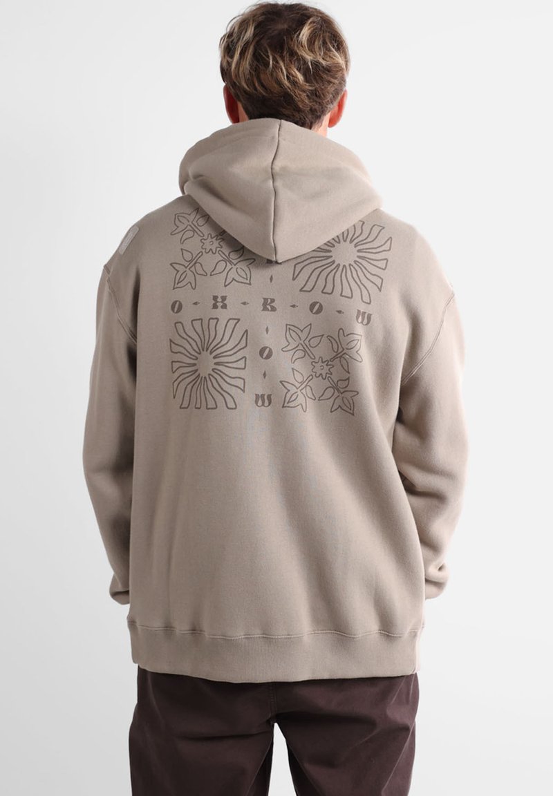 Haut à capuche beige avec cordon de serrage. Présente un motif graphique texturé en marron, incluant des fleurs et des formes de soleil au dos.