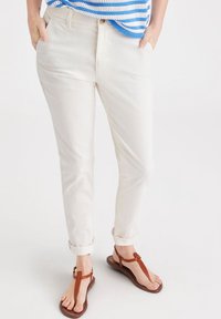 Beiga bomullshängande byxor med avsmalnande passform och rullade fållar, tillsammans med bruna platta sandaler. Toppens design har blå och vita ränder.