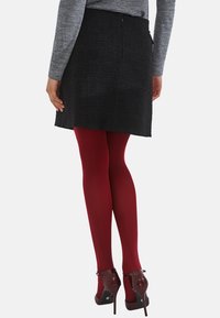 Czarna spódnica o teksturowanym materiale, w prostym kroju, zestawiona z bordowymi rajstopami i eleganckimi bordowymi szpilkami. Widok z tyłu podkreśla pas i zamek.