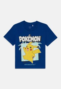 Blå bomull T-skjorte med et Pikachu-trykk med teksten "POKÉMON" over og "GOTTA CATCH 'EM ALL!" under, satt mot en lys bakgrunn.
