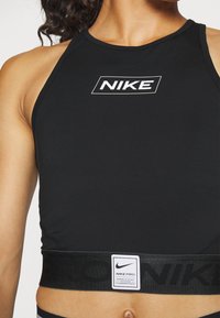 Top corto sportivo nero realizzato in tessuto elasticizzato. Presenta un logo Nike bianco sulla parte frontale e un elastico brandizzato nero nella parte inferiore.