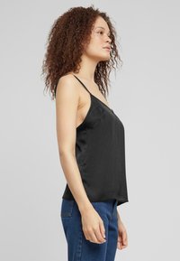 Camisole nera in satin con spalline sottili, design a V e una texture liscia. Abbinata a jeans blu, mette in risalto uno stile minimalista.