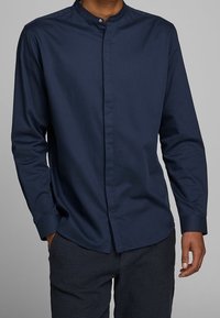 Camicia a maniche lunghe blu navy con colletto alla mandarino. Realizzata in tessuto morbido, presenta una chiusura con bottoni e polsini aderenti.