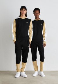 Set atletico nero e beige caratterizzati da maniche lunghe, pannelli a contrasto, scollatura rotonda e accenti con logo, abbinati a sneakers bianche.