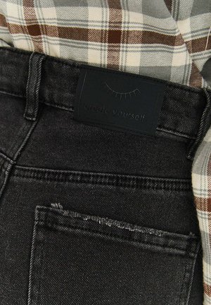 Schwarze Denim-Jeans mit strukturierter Oberfläche, ausgestattet mit einem dunklen Markenlabel am Bund, teilweise bedeckt von einem braunen karierten Hemd.
