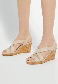 Beige wedge sandalen met een kurken hak, voorzien van een kruisband ontwerp en een open teen. Gladde lederen textuur met een verstelbare enkelband.