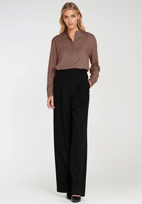 Brązowa bluzka z długim rękawem i kołnierzykiem, zestawiona z czarnymi spodniami o wysokim stanie z plisami. Gładki materiał o luźnym kroju.
