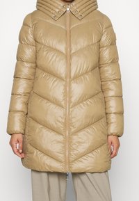 Cappotto puffer beige con un motivo a losanga, ampio colletto e chiusura con zip. Presenta una finitura lucida e polsini elasticizzati.